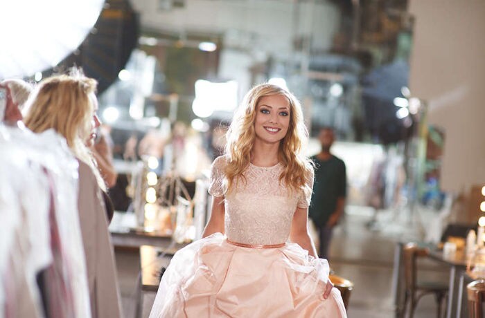A woman in a light pink gown is smiling towards the camera, revealing her bright white un-stained teeth. 